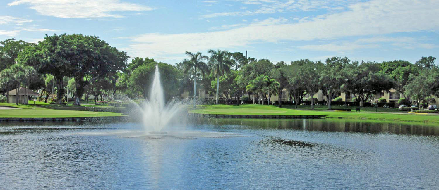 There are many trees on the golf course, and a lake with a fountain.