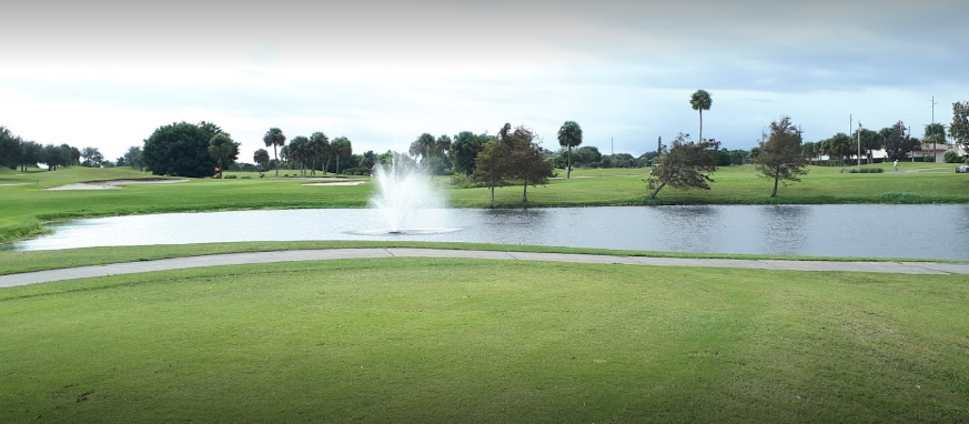 On the golf course, there is a lake with a fountain and many trees