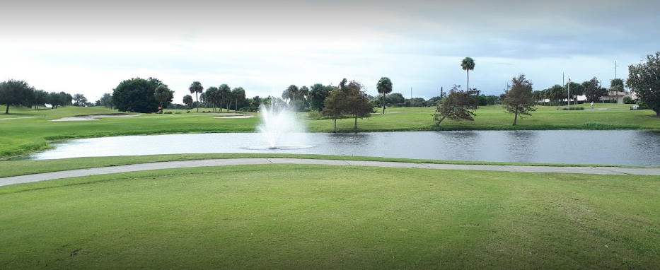 On the golf course, there is a lake with a fountain and many trees