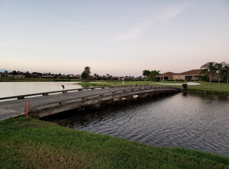 There is a lake with a bridge and many homes on the golf course